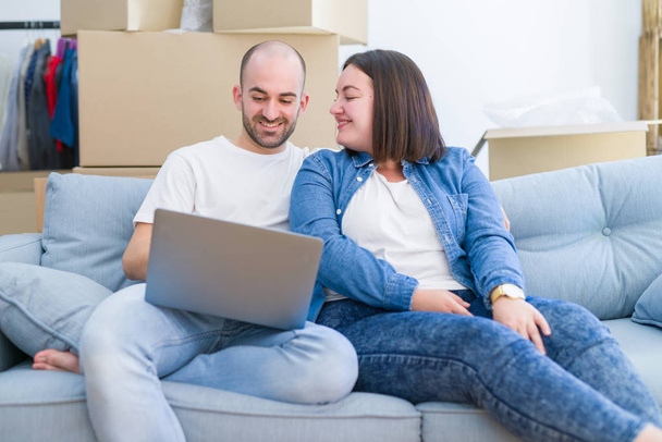 Jovem casal sentado no sofá em nova casa usando computador lapt
 - Foto, Imagem