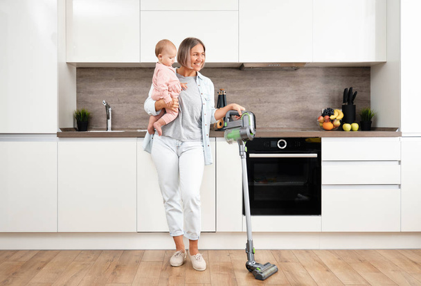 Vacuuming and Cleaning the House. Happy mother with her Baby in her Arms. Parenthood and motherhood. Caring woman with child. Housework - Фото, изображение