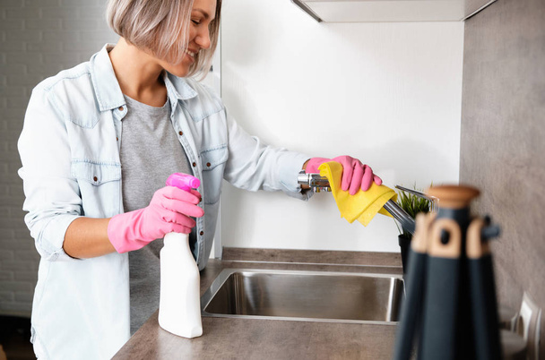 掃除をする女。黄色のスポンジと洗剤でキッチンを洗う.家の掃除 - 写真・画像