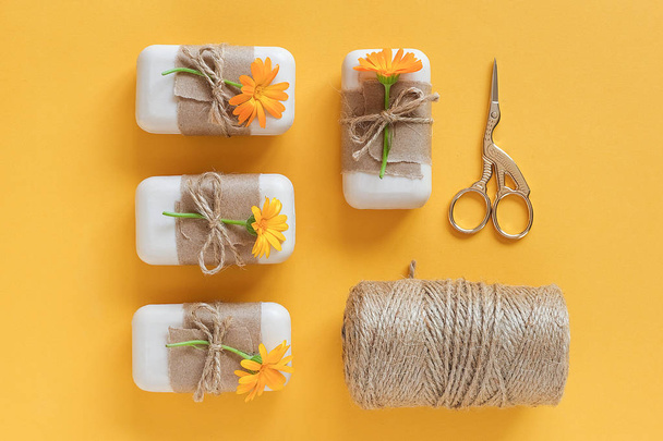 Handmade natural soap set decorated with craft paper, orange calendula flowers, skein of twine and scissors on yellow background . Organic cosmetics concept. Top view Flat lay Template for design - Valokuva, kuva