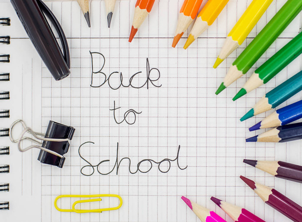 Επιστροφή στο σχολείο ιδέα-μολύβια ουράνιο τόξο, στυλό, συνδετήρας ντοσιέ και κλιπ χαρτιού στο πλέγμα χαρτιού πλέγματος με "επιστροφή στο σχολείο" γραμμένο σε αυτό - Φωτογραφία, εικόνα