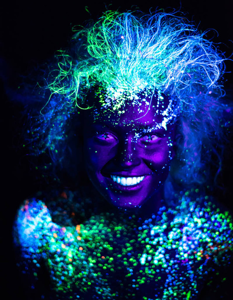 Body art and contact lenses glowing in ultraviolet light. Woman smiling, painted in fluorescent powder. Stars in the eyes - Photo, Image