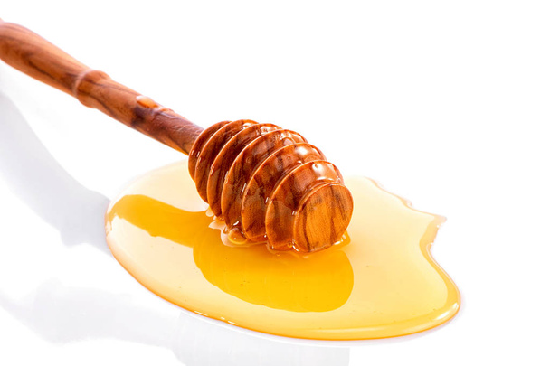 wooden dipper in liquid honey close-up on white background with reflection   - Foto, Imagen