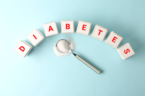 Kubussen vormen woord Diabetes en lepel met suiker op kleur achtergrond - Foto, afbeelding