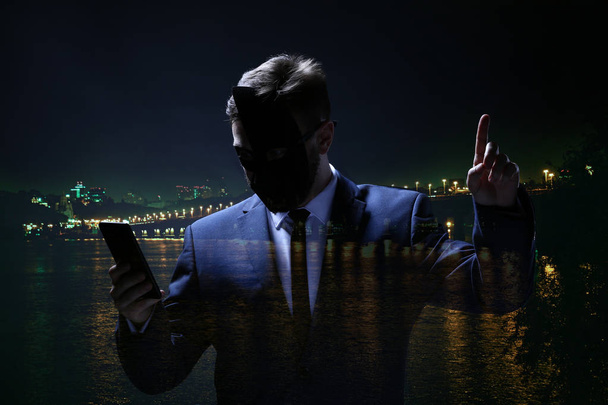 Dubbele blootstelling van professionele hacker met mobiele telefoon en stad 's nachts - Foto, afbeelding
