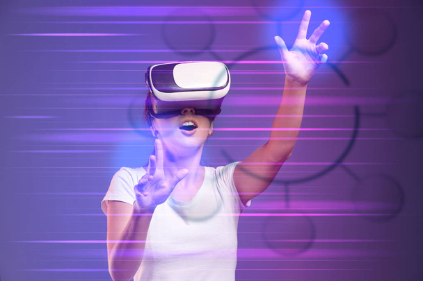 Mladá žena, která nosí ve VR brýle a používá virtuální obrazovku na tmavém pozadí - Fotografie, Obrázek