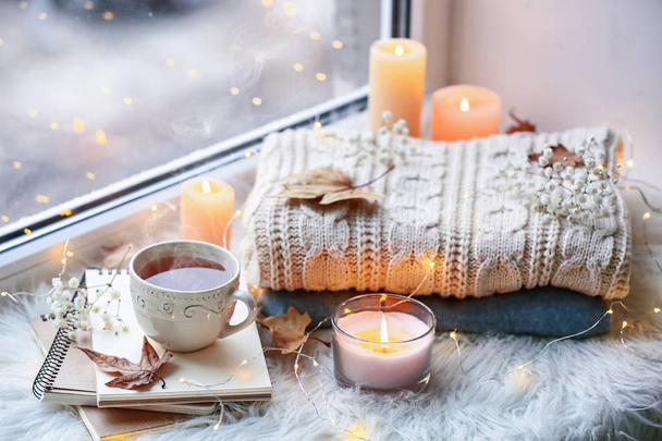 Hermosa composición con velas encendidas y taza de té caliente en el alféizar de la ventana
 - Foto, imagen