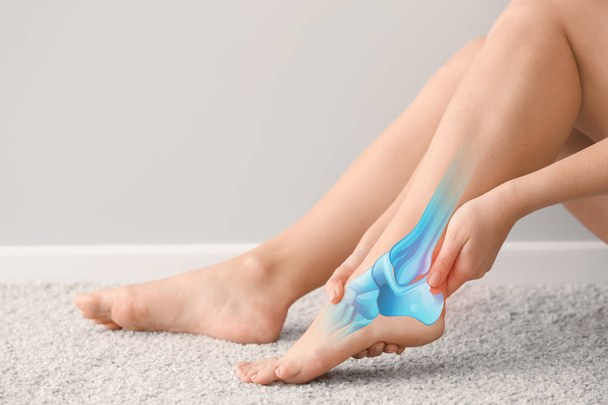 Frau leidet unter Schmerzen im Bein, während sie auf Teppich sitzt - Foto, Bild