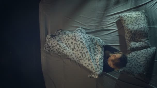 Η γυναίκα πάει για ύπνο. Κάτοψη. Μια γυναίκα κάθεται σε ένα μεγάλο κρεβάτι. Ξαπλώνει, σκεπάζεται με μια κουβέρτα και ετοιμάζεται να κοιμηθεί.. - Πλάνα, βίντεο