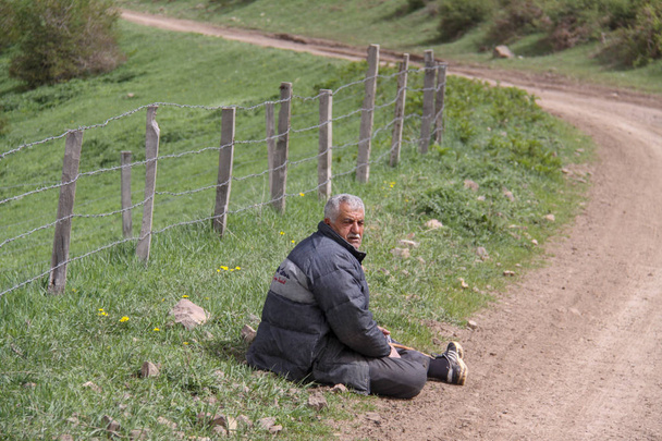 A fáradt vidéki ember ül az út mellett a padlón, egy gazdaság van zárva egy kerítés, Irán, Gilan - Fotó, kép