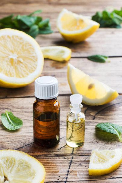 Essential lemon oil in bottle, fresh fruit slices on wooden back - Fotó, kép