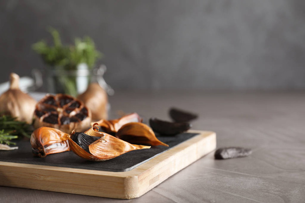 Board with black garlic on grey table. Space for text - 写真・画像