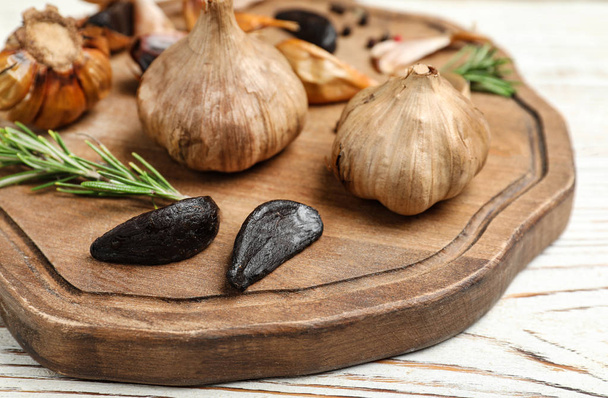 Board with tasty black garlic on white wooden table - Φωτογραφία, εικόνα
