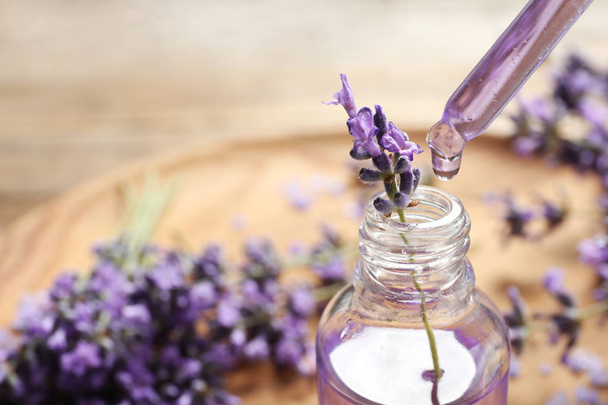 Natuurlijke olie druipend in fles en lavendel bloemen op tafel, close-up met ruimte voor tekst. Cosmetisch product - Foto, afbeelding