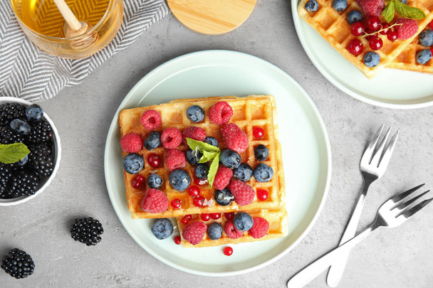 Flat lay composition with delicious waffles and fresh berries on grey table - Zdjęcie, obraz