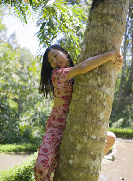 Genç güzel ve eğlenceli Asyalı Çinli kadın yaz yaşam tarzı portre tırmanma ve sarılma ağaç gövde ve tropikal ahşap doğanın mutlu güzelliği zevk  - Fotoğraf, Görsel