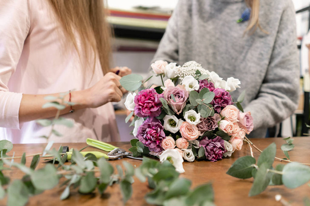 Close-up flowers in hand. Florist workplace. Woman arranging a bouquet with roses, carnation and other flowers. A teacher of floristry in master classes or courses - Photo, Image
