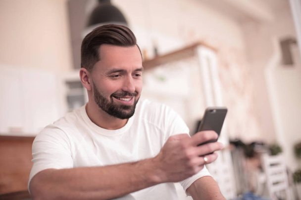 attractive man reading an SMS while sitting and kitchen - Фото, зображення