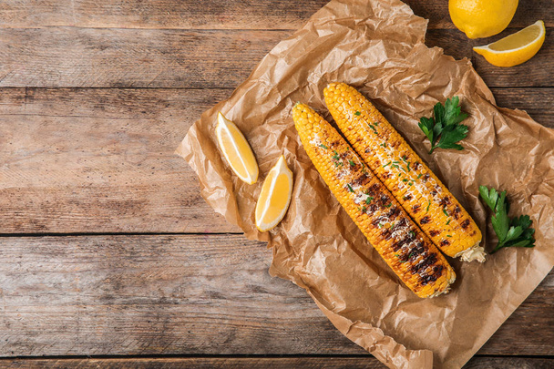 Flat lay composition of grilled corn cobs on wooden table. Space for text - Foto, Bild