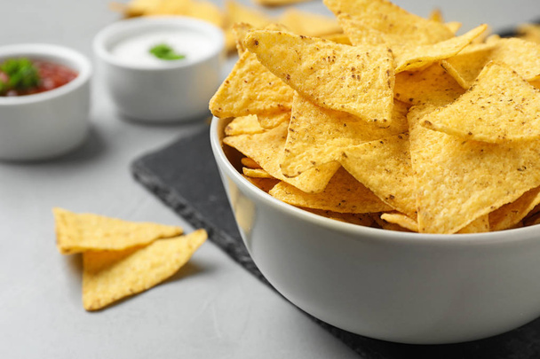 Bowl with tasty Mexican nachos chips on grey table, closeup view. Space for text - Fotó, kép