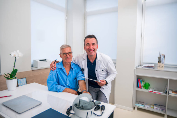 Un médico humilla a su paciente mayor mientras ambos sonríen mientras ambos sonríen.  - Foto, Imagen