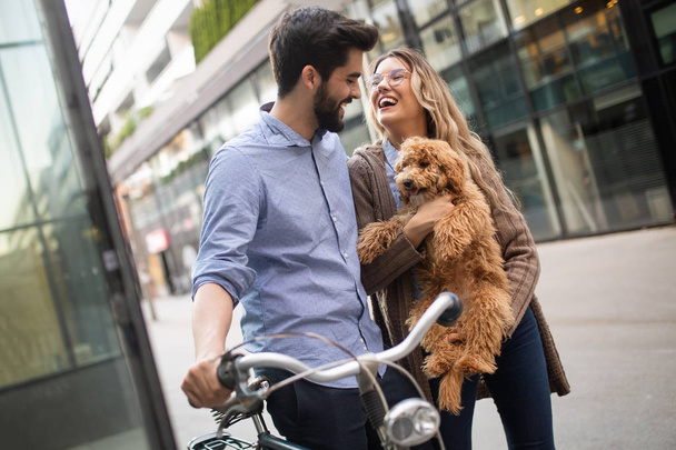Young couple on a bike ride on a sunny day in the city with dog - Фото, изображение