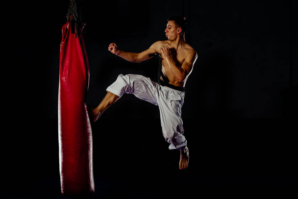 Мускулистый парень совершенствует свои боксерские навыки над красной тяжелой сумкой
 - Фото, изображение