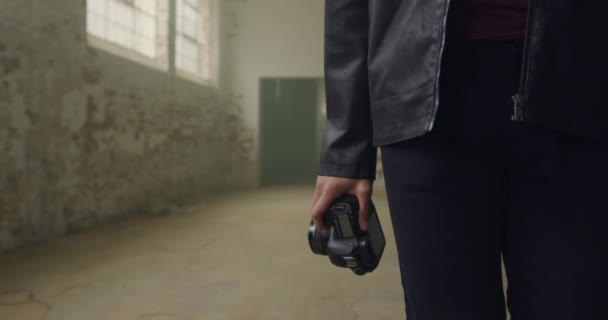 Front view mid section of a hip young mixed race man in an empty warehouse, walking and carrying a camera - Záběry, video