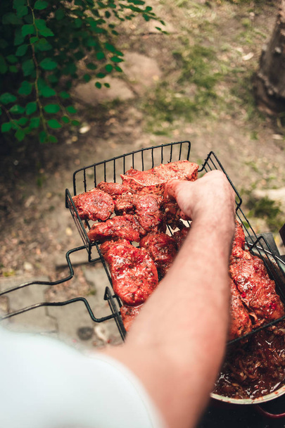 Man puts marinated meat on a metal grid - Photo, Image