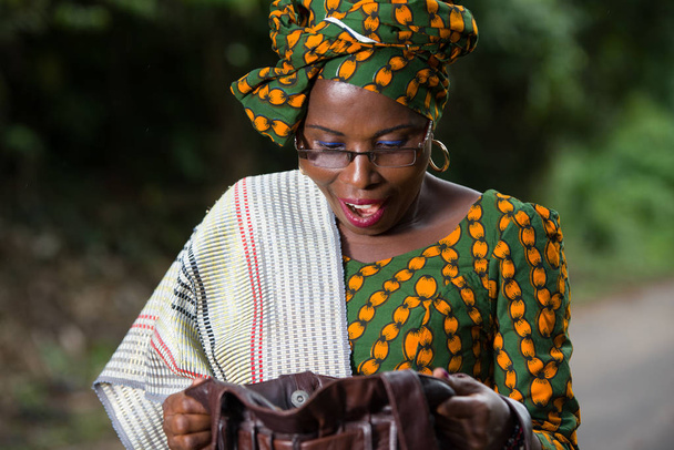 νεαρή αφρικανική γυναίκα στέκεται σε παραδοσιακά ρούχα και γυαλιά ψάχνει για κάτι σε τσάντα μακιγιάζ - Φωτογραφία, εικόνα