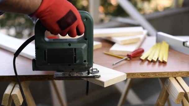 O carpinteiro de artesão adulto com as mãos protegidas por luvas trabalha com a serra elétrica para cortar uma mesa de madeira. Tarefa de casa, faça você mesmo. Filmagem
. - Filmagem, Vídeo