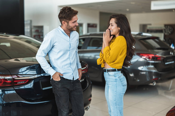 beautiful young couple man and woman choosing which car to buy in dealership center - Valokuva, kuva