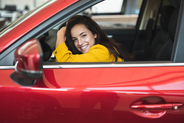 beautiful brunette woman looking for new car in dealership center checking the vehicle interior - Фото, изображение