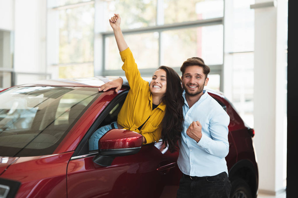 young couple looking for car in dealership center beautiful brunette woman is sticking out the vehicle window and handsome man is standing near smiling - Foto, immagini