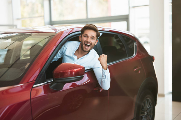 young handsome man looking for new car in dealership center sticking out the vehicle window - Foto, Imagem