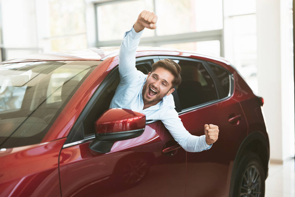 young handsome man looking for new car in dealership center sticking out the vehicle window happily - Фото, изображение