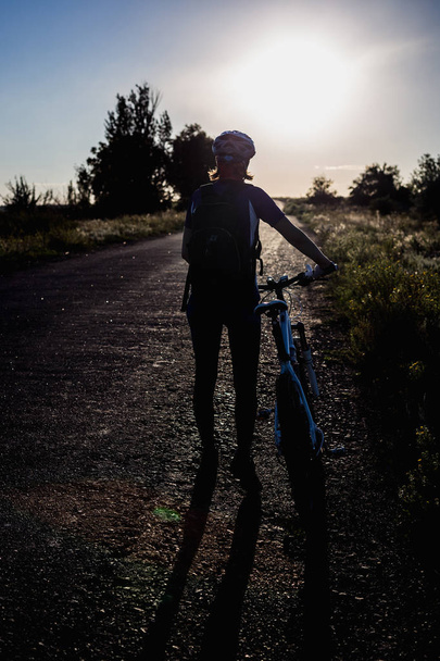 Silhouette eines Mädchens mit Fahrrad bei Sonnenuntergang im Sommer - Foto, Bild
