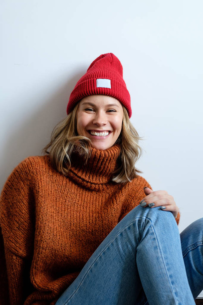 Portrait of a girl in a sweater and a red hat on a white wall background - Fotoğraf, Görsel