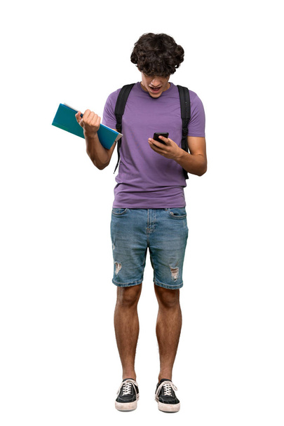 Ένα πλήρες πλάνο ενός νεαρού μαθητή που εξέπληξε και στέλνει ένα μήνυμα πάνω από απομονωμένο λευκό φόντο - Φωτογραφία, εικόνα