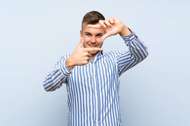 Young handsome blonde man over isolated blue background focusing face. Framing symbol - Photo, image