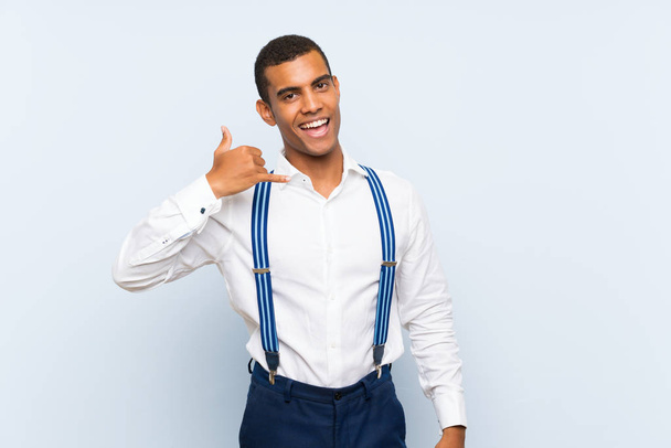 Young handsome brunette man with suspenders over isolated background making phone gesture - Foto, imagen