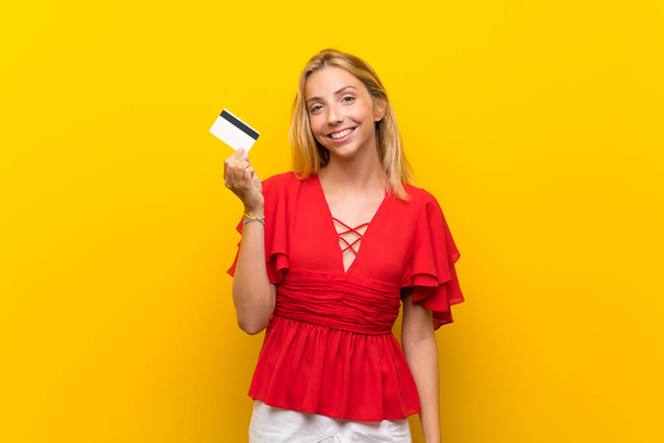 Блондинка на изолированном желтом фоне держит кредитку
 - Фото, изображение