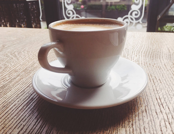 Ένα φλιτζάνι ζεστό καπουτσίνο σε μια καφετέρια, καφέ σε ένα ξύλινο τραπέζι που - Φωτογραφία, εικόνα