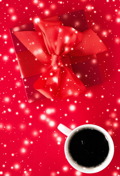 Winter vakantiegift box, koffie kopje en gloeiende sneeuw op rode platte - Foto, afbeelding
