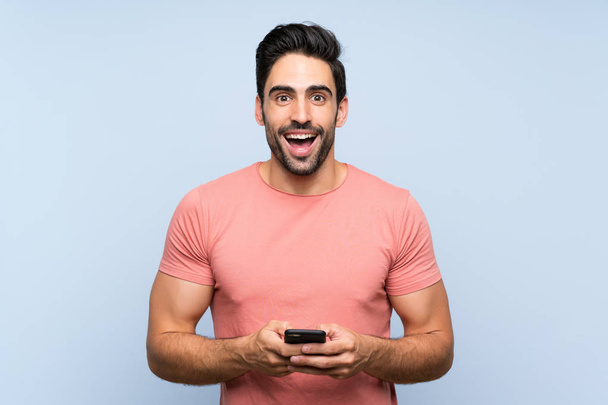 Hombre joven guapo en camisa rosa sobre fondo azul aislado sorprendido y enviando un mensaje
 - Foto, Imagen