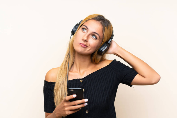 Mujer rubia joven escuchando música con un móvil sobre un fondo aislado
 - Foto, Imagen
