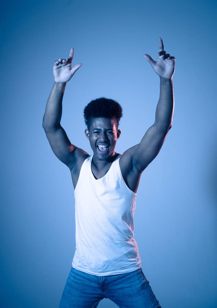 Portrait of inspired cool african american teenager man dancing feeling the music and enjoying life on blue moody disco neon light background. In People, Youth Party night lifestyle. Studio shot. - Fotó, kép