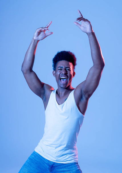 Portrait of inspired cool african american teenager man dancing feeling the music and enjoying life on blue moody disco neon light background. In People, Youth Party night lifestyle. Studio shot. - Fotografie, Obrázek