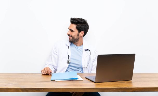 Jeune homme médecin avec son ordinateur portable sur un mur isolé regardant sur le côté
 - Photo, image