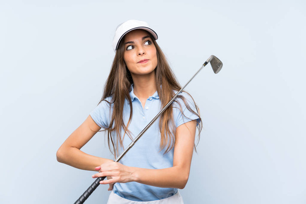 Joven golfista mujer sobre aislada pared azul mirando hacia arriba mientras sonríe
 - Foto, Imagen